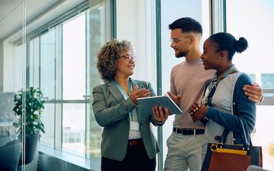 A woman is holding a tablet and talking to a man and woman.