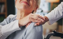 An elderly woman in a wheelchair is being comforted by a nurse.