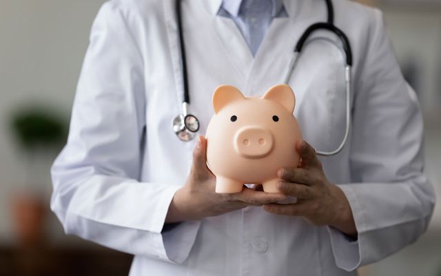 A doctor is holding a piggy bank with a stethoscope around his neck.