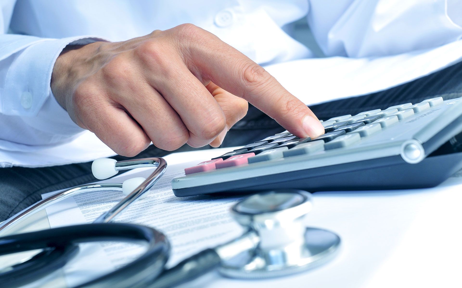 A doctor is using a calculator next to a stethoscope.