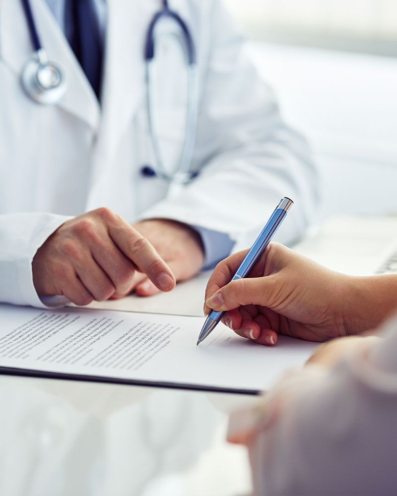 A doctor is talking to a patient who is writing on a piece of paper.