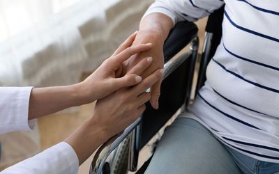 A woman in a wheelchair is holding another woman 's hand.