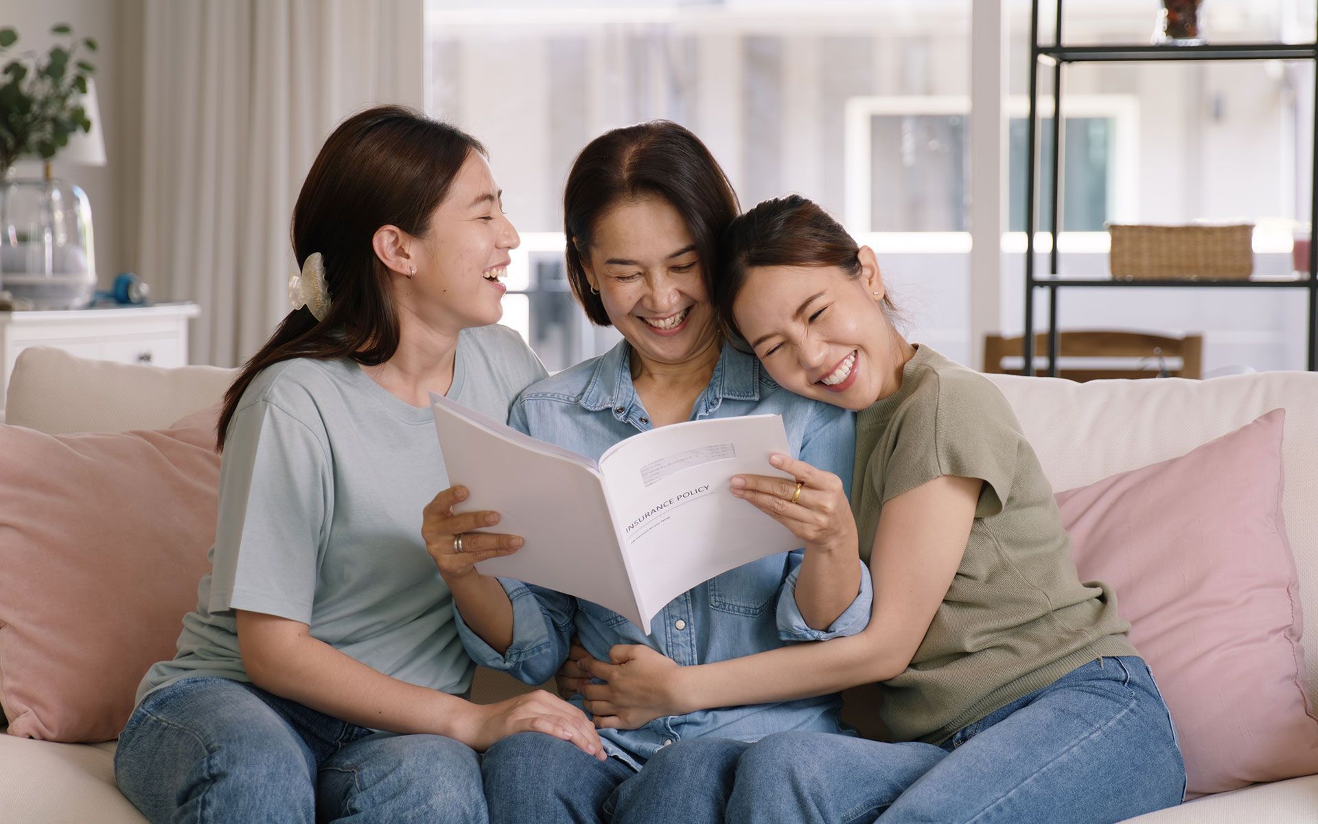 Three women are sitting on a couch reading a book together.