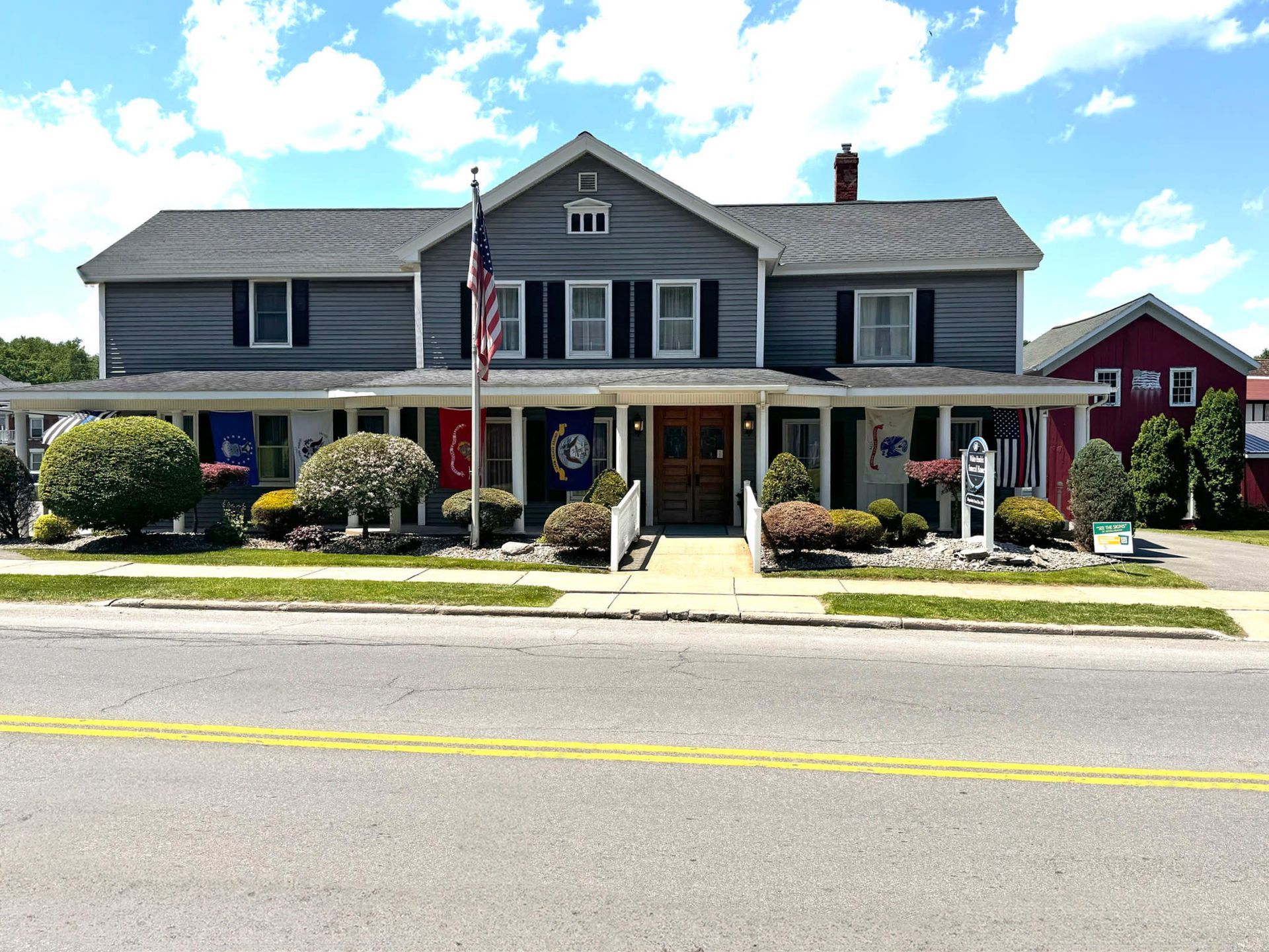 A large house with a flag on the front of it is sitting on the side of the road.