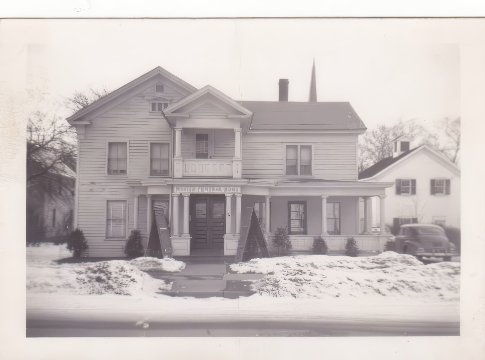 A black and white photo of a large house in the snow