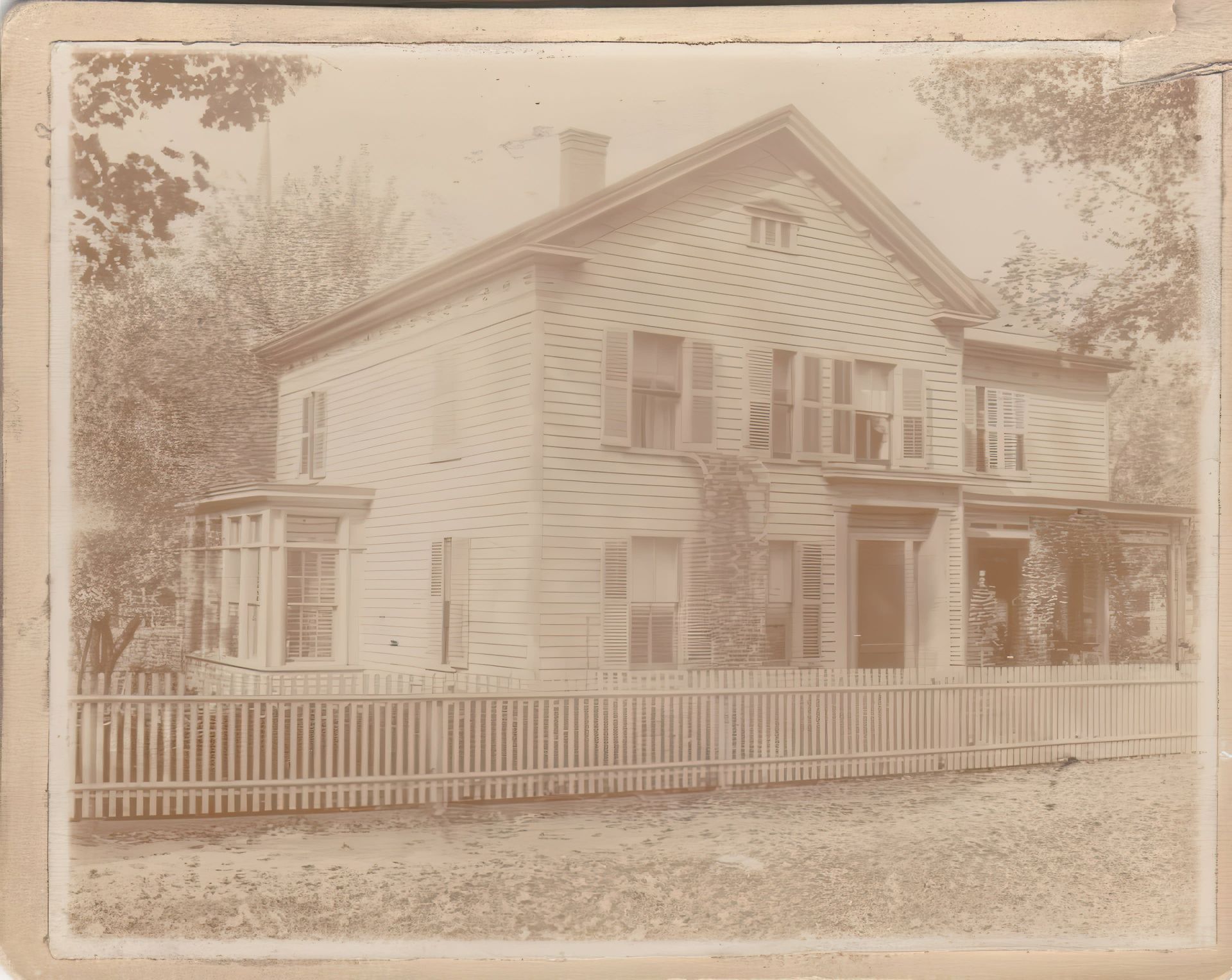 A black and white photo of a house with a white picket fence