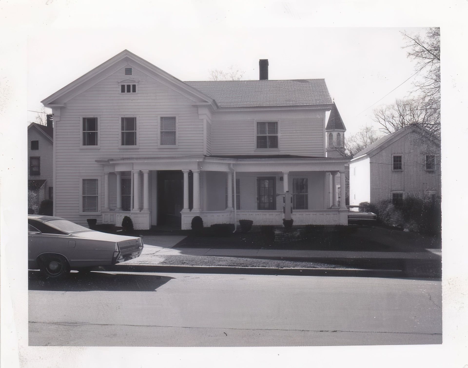 A black and white photo of a house with a car parked in front of it