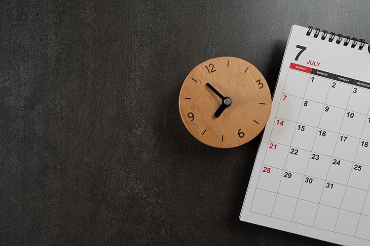 A wooden clock is sitting next to a calendar on a table.