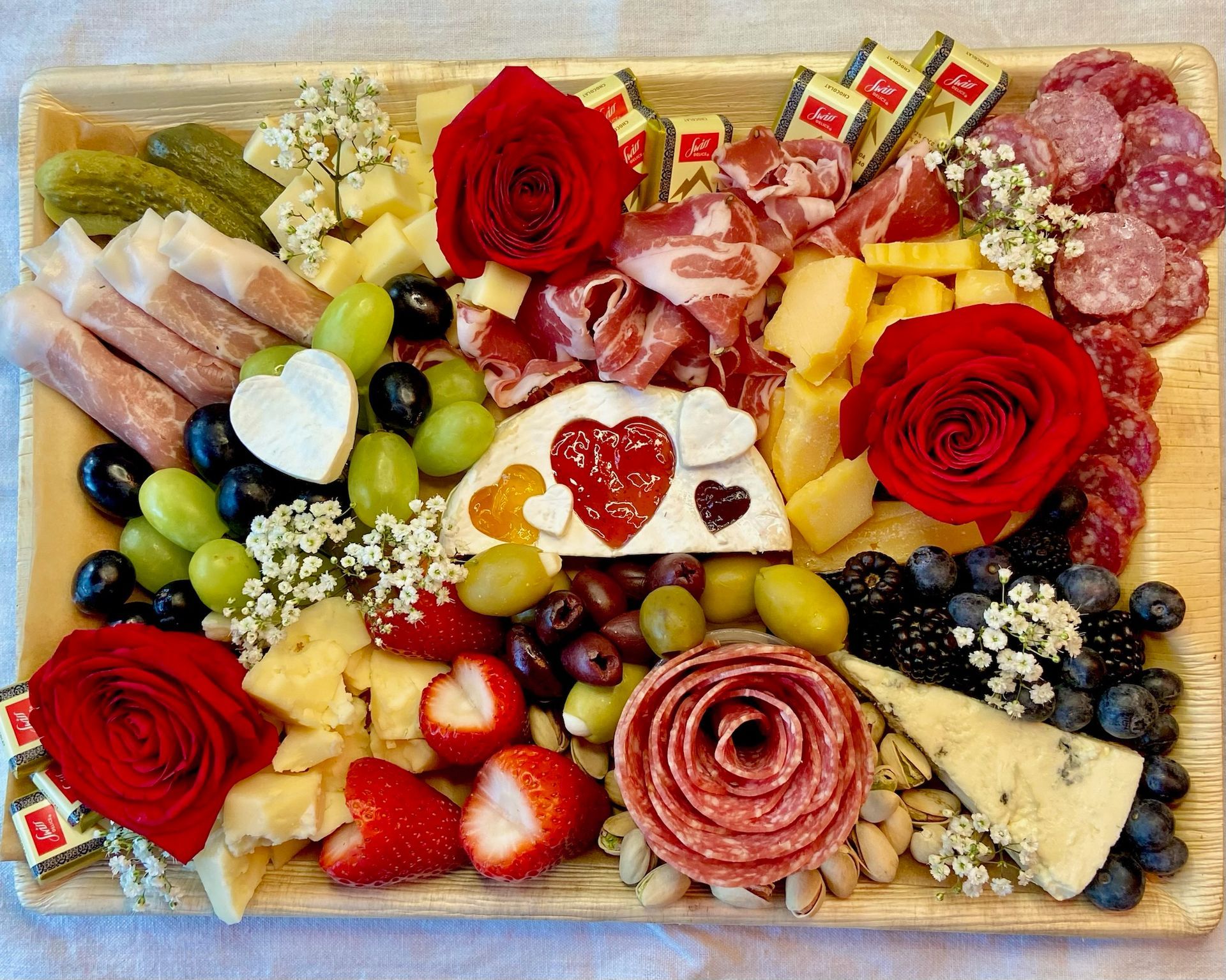 A wooden cutting board filled with meat , cheese , fruit and flowers.