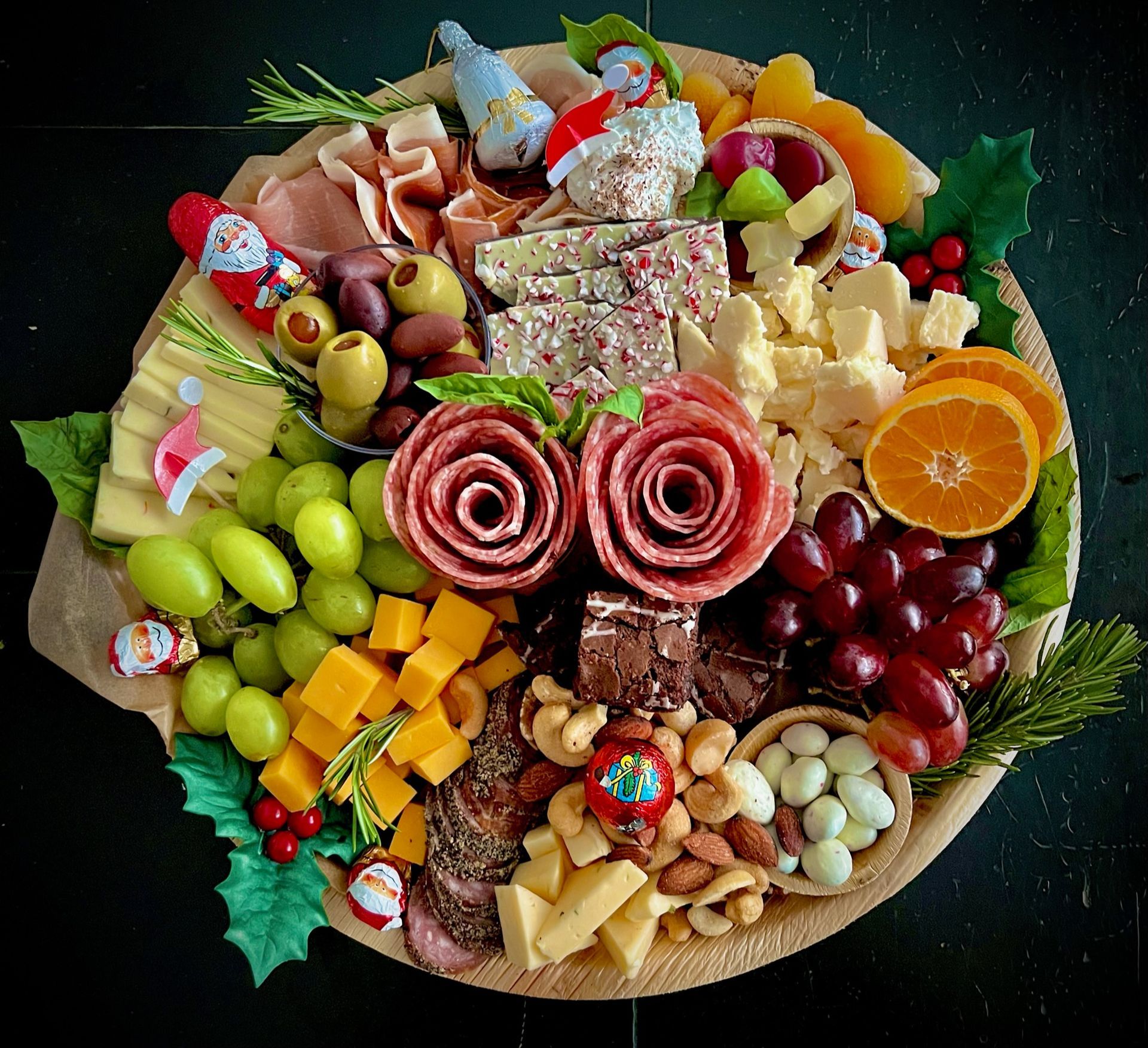 A wooden cutting board filled with meat , cheese , grapes , nuts and fruit.