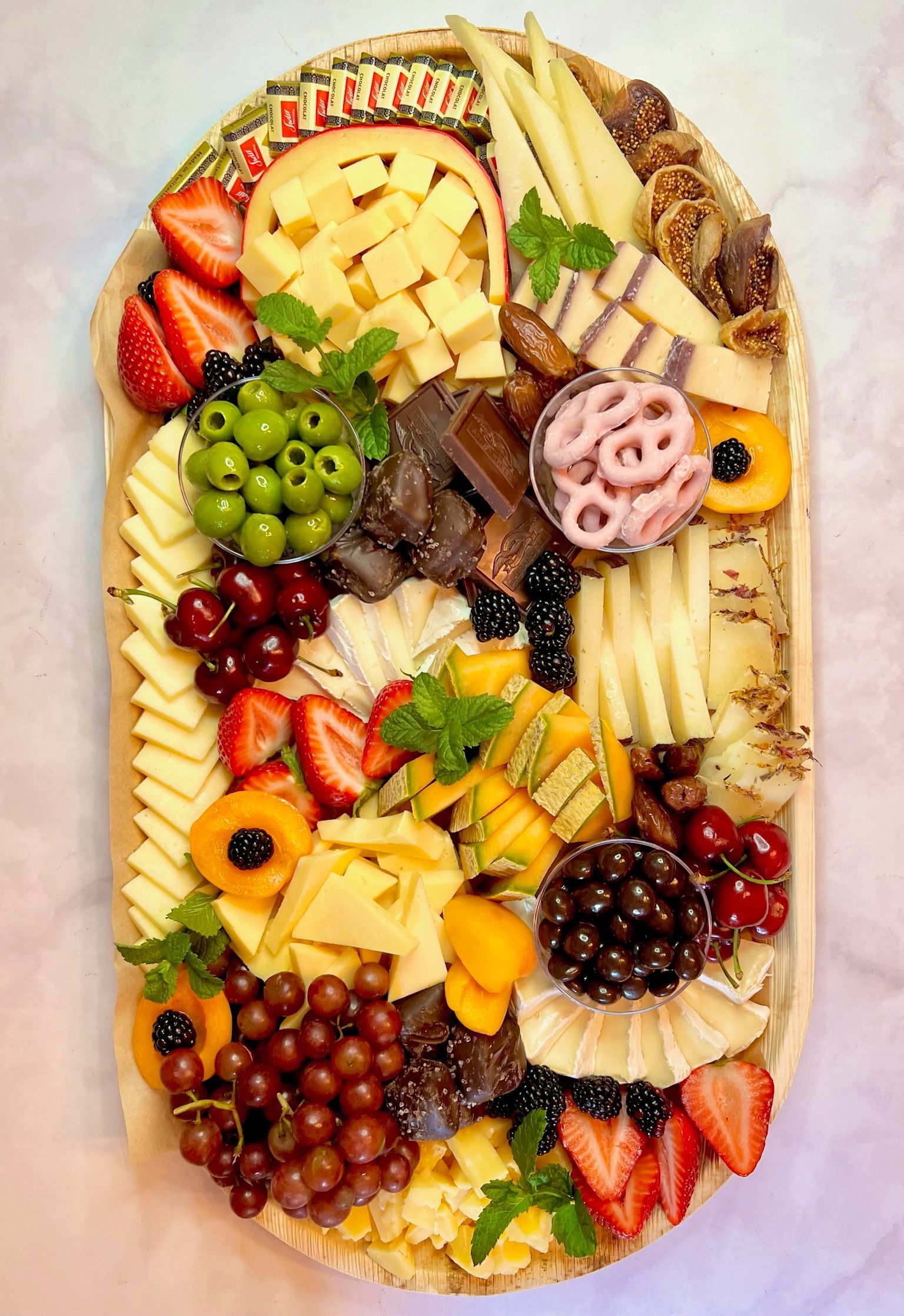 A large oval shaped platter filled with fruit , cheese , and nuts.