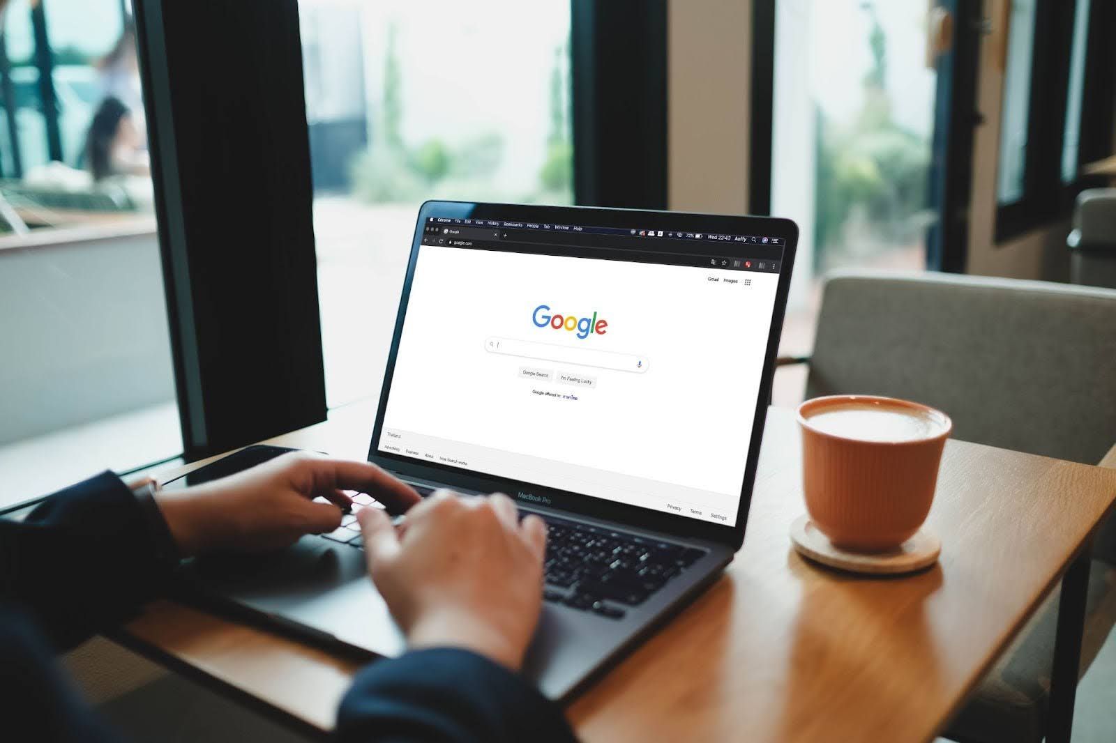 A person is typing on a laptop computer while sitting at a table with a cup of coffee.