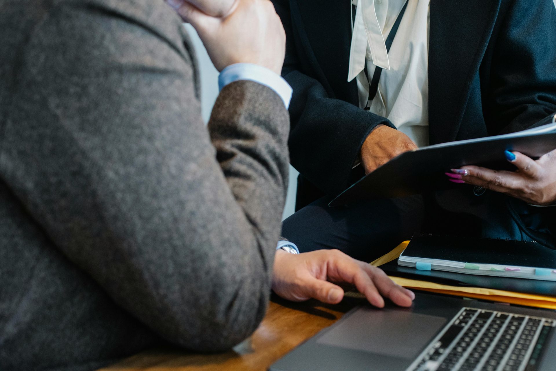 Person in a suit interacting with another person holding documents, focused on a laptop.
