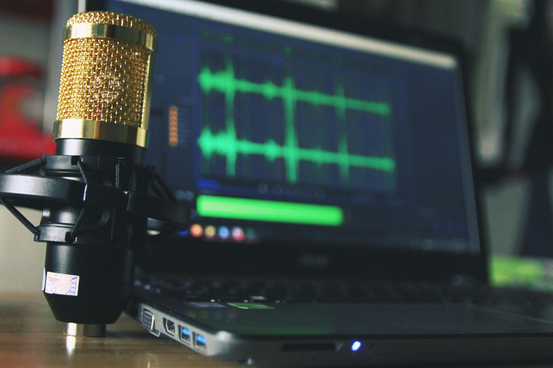 Gold microphone in front of a laptop displaying audio waveforms, suggesting recording or editing.