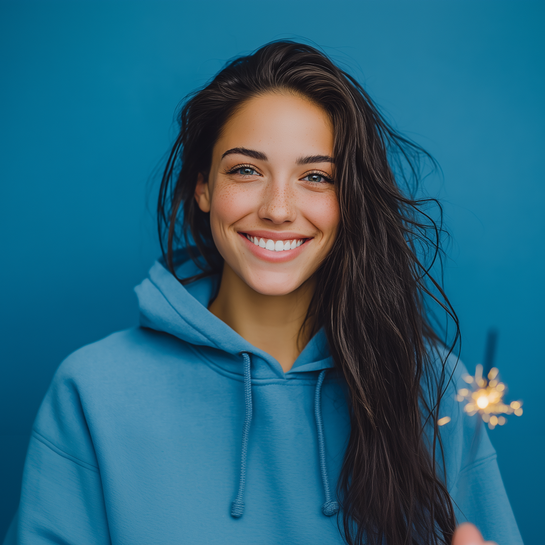 Woman in blue hoodie smiles with a lit sparkler against a blue backdrop.