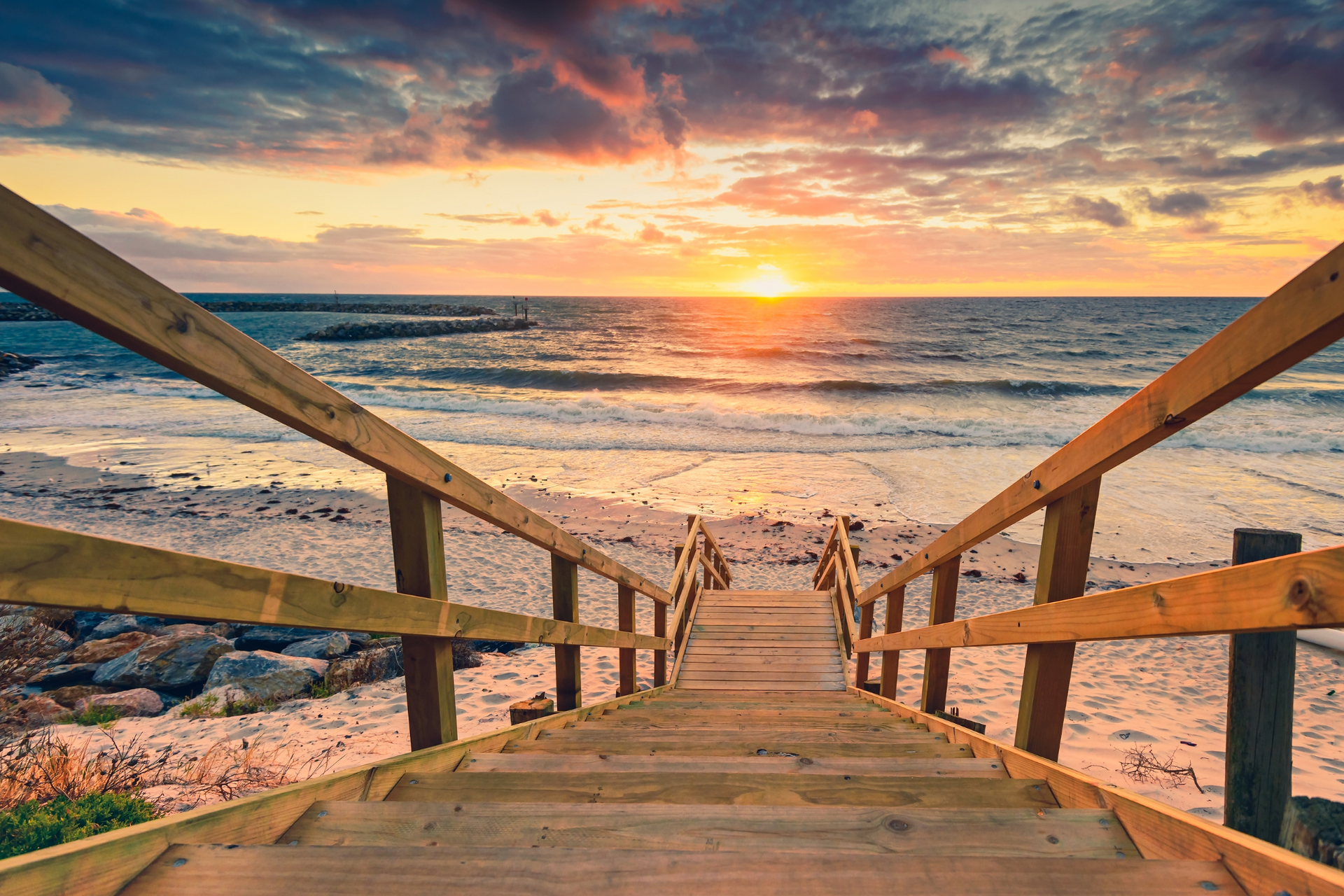 A wooden staircase leading to the beach at sunset.