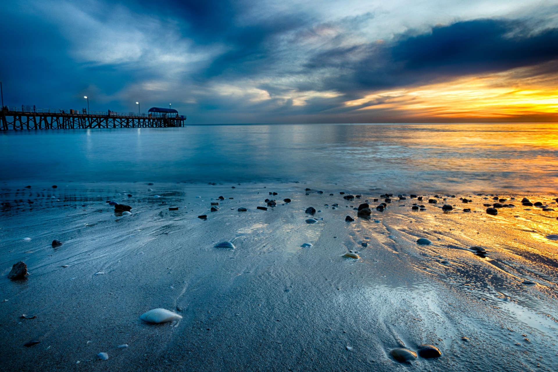 A beach with a pier in the background at sunset.