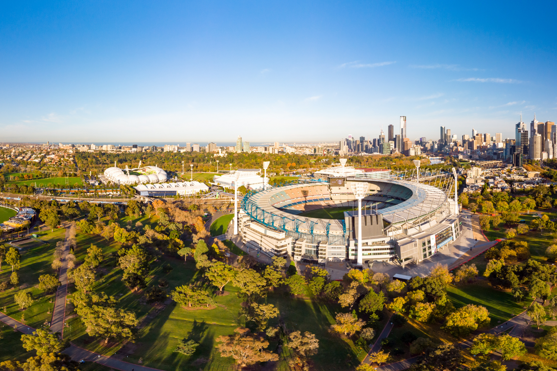 An aerial view of a large stadium surrounded by trees and a city skyline.
