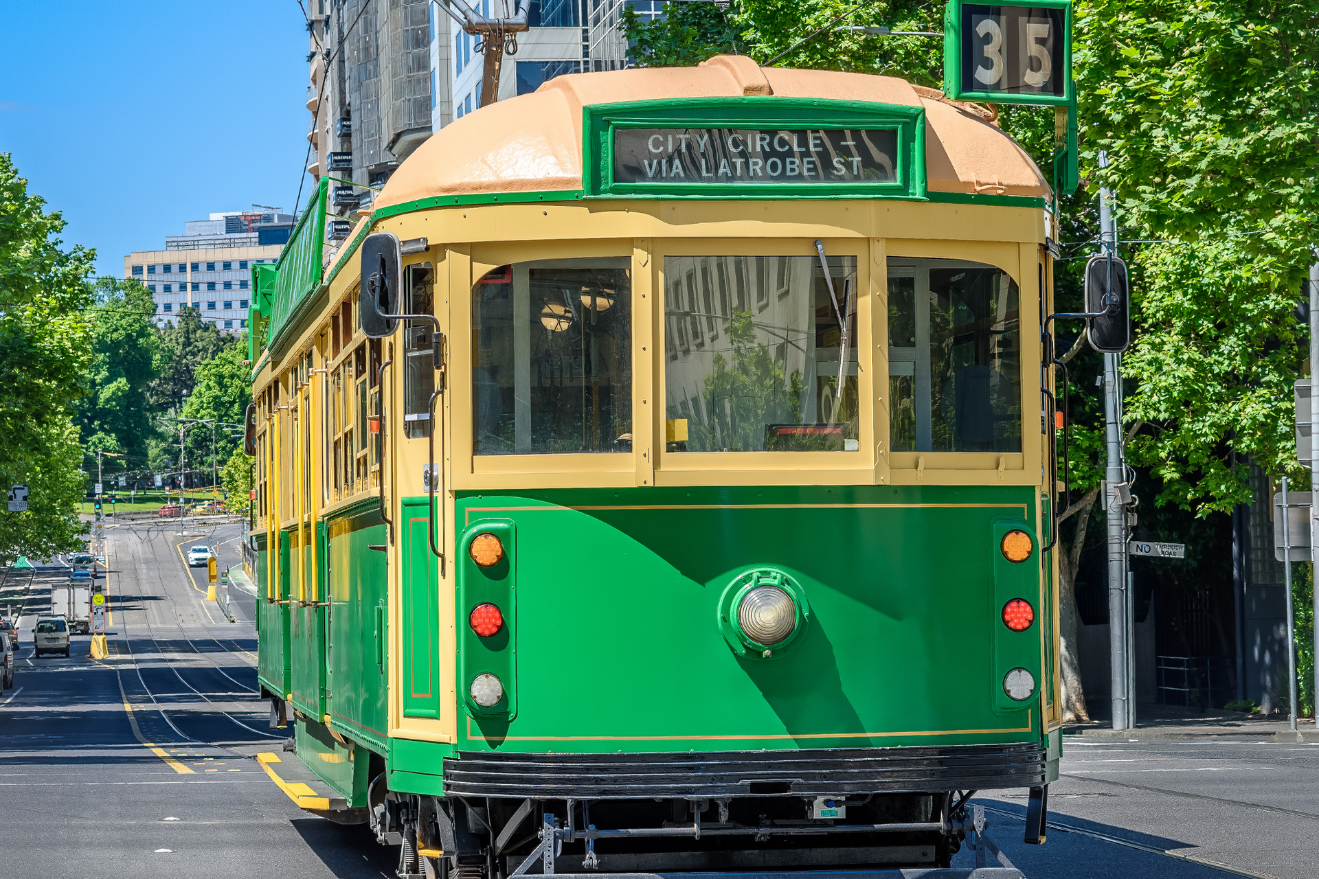A green and yellow trolley is driving down a city street.