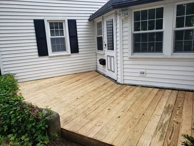 a wooden deck is in front of a white house with black shutters