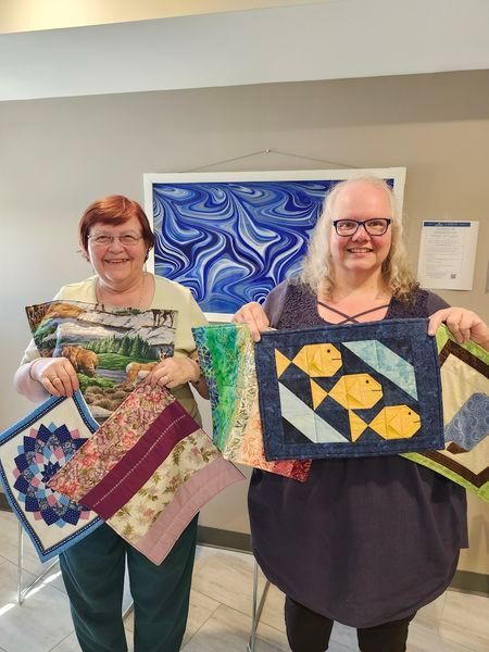Two women are holding quilts in their hands and smiling