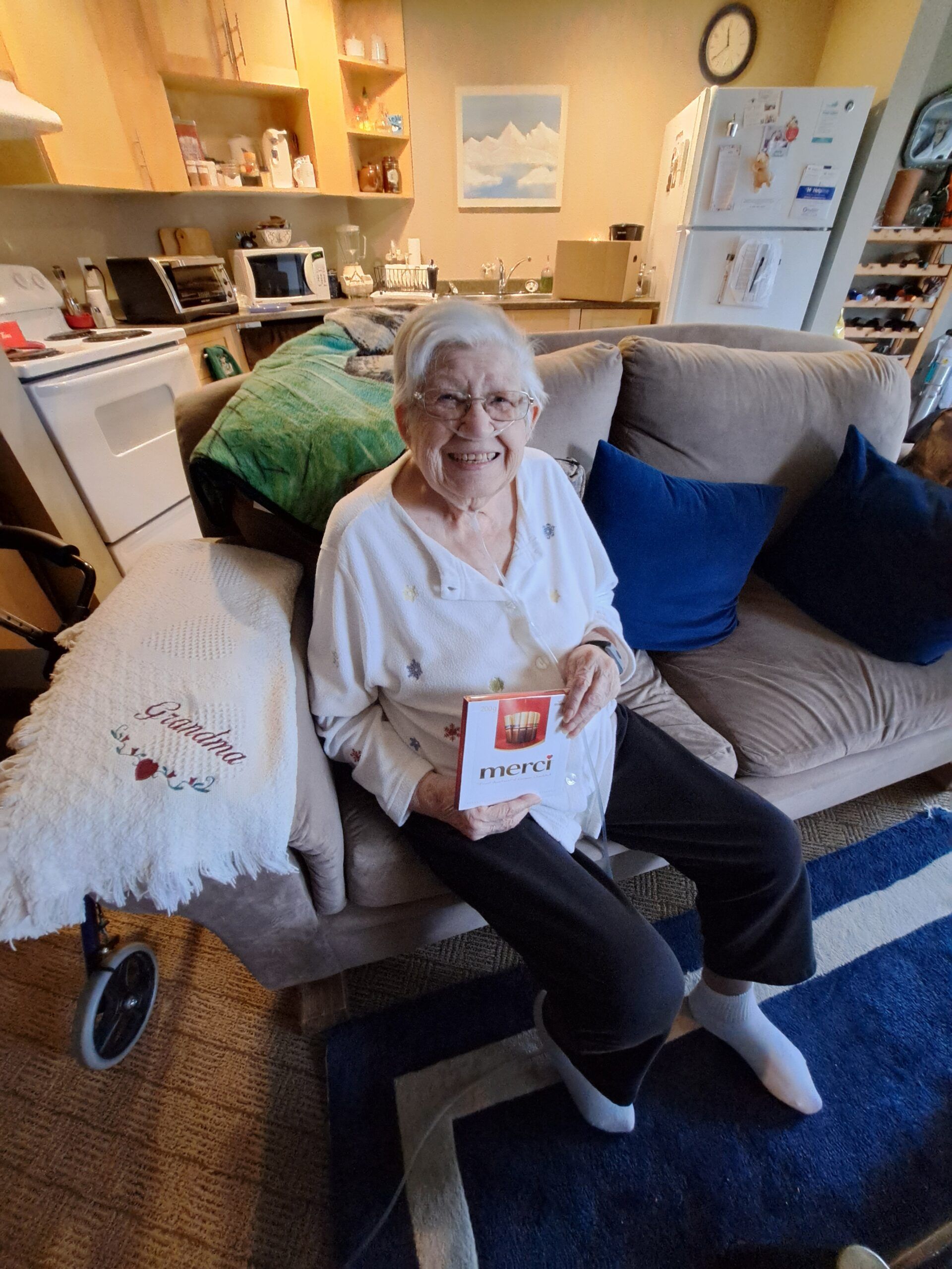 An elderly woman is sitting on a couch holding a card.