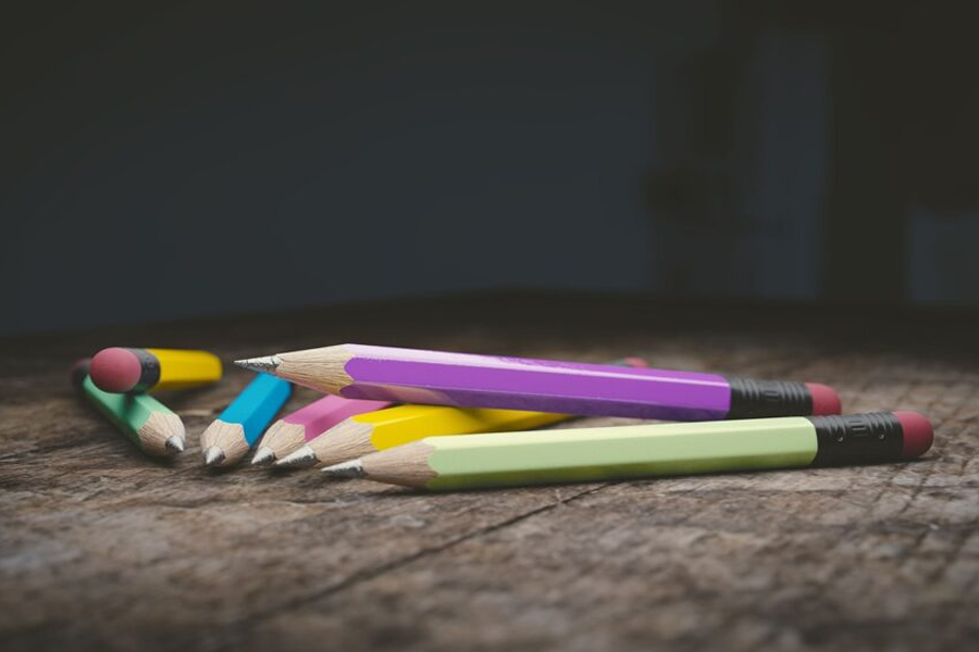 A bunch of colorful pencils are laying on a wooden table.