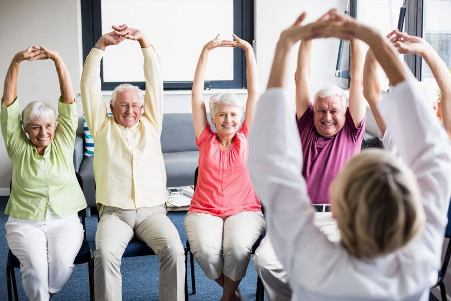 A group of elderly people are sitting in chairs doing stretching exercises.