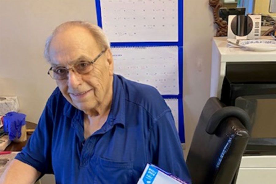 An elderly man in a blue shirt is sitting at a desk holding a box.