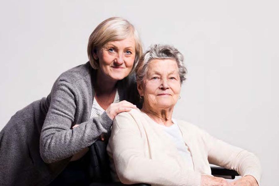 A woman is standing next to an older woman in a wheelchair.