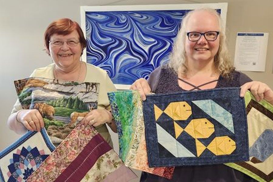 Two women are holding quilts in their hands and smiling.