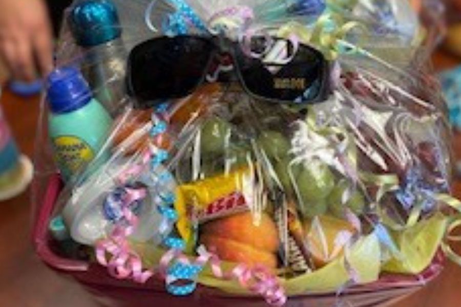 A basket filled with fruit , candy , sunglasses and a bottle of sunscreen.