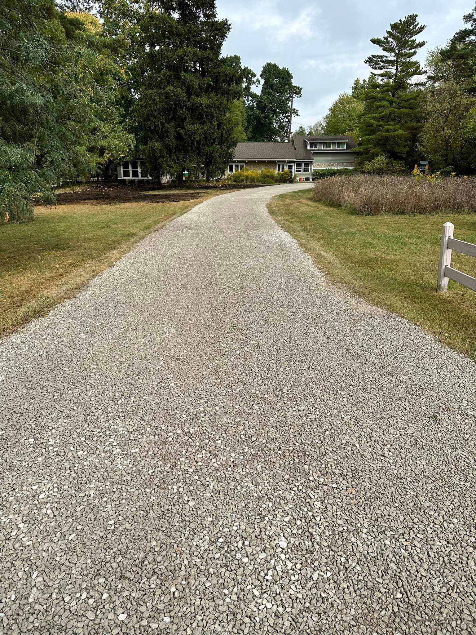 A gravel driveway leading to a house surrounded by grass and trees.