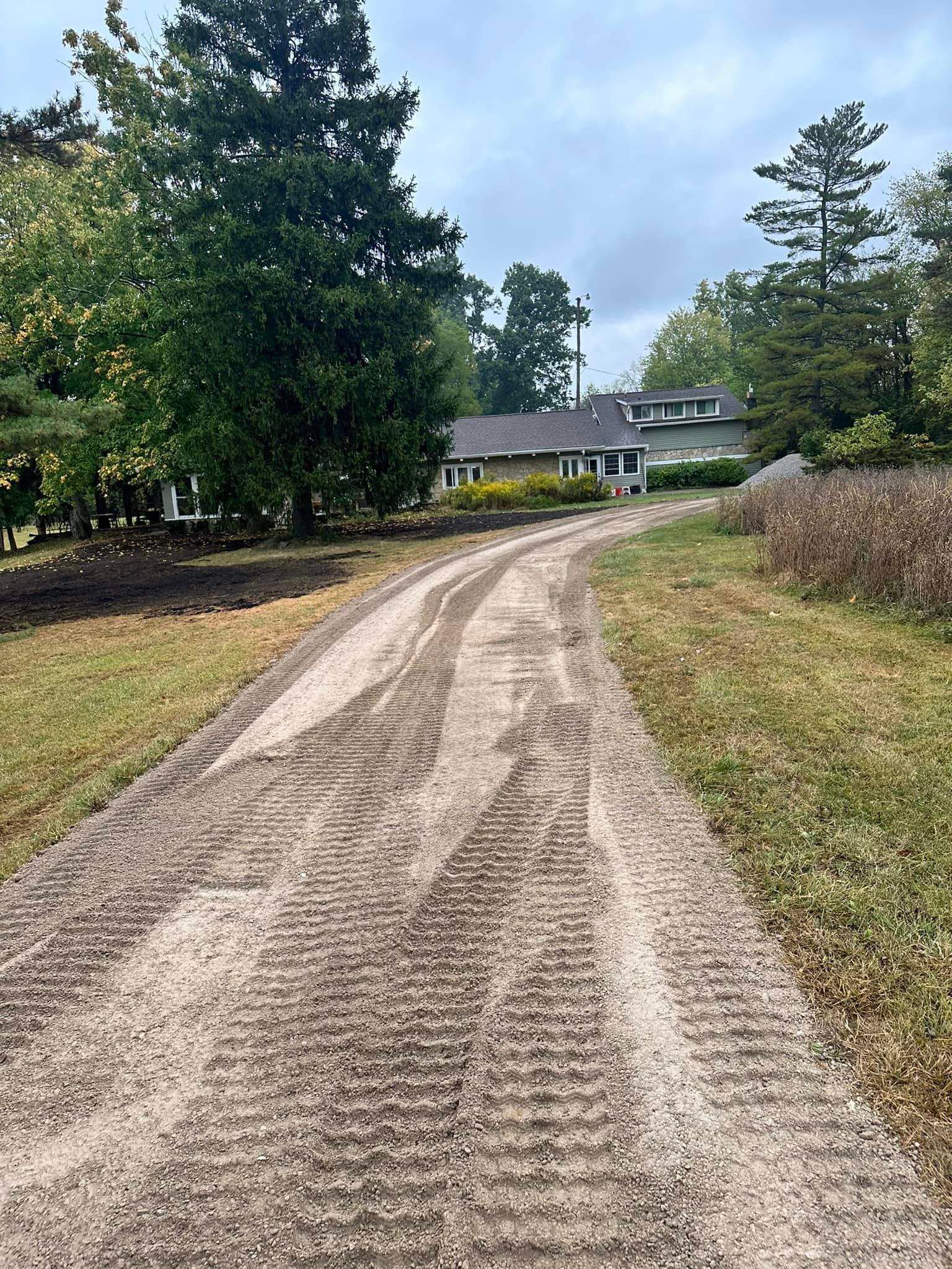 A dirt road leading to a house surrounded by trees and grass.