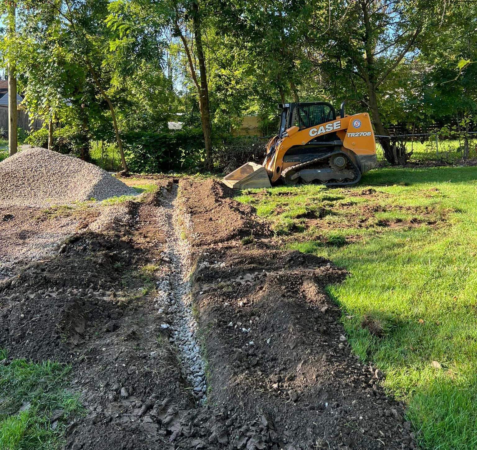 A bulldozer is digging a trench in a grassy field.