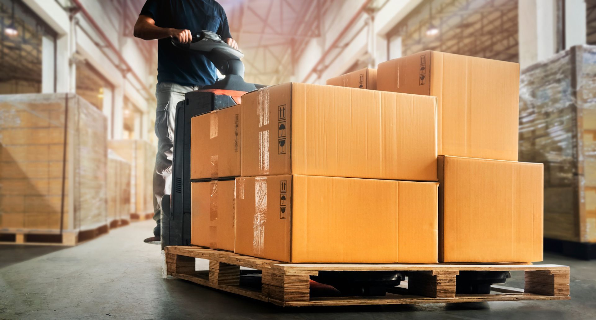 A man is riding a forklift in a warehouse with boxes on a pallet.