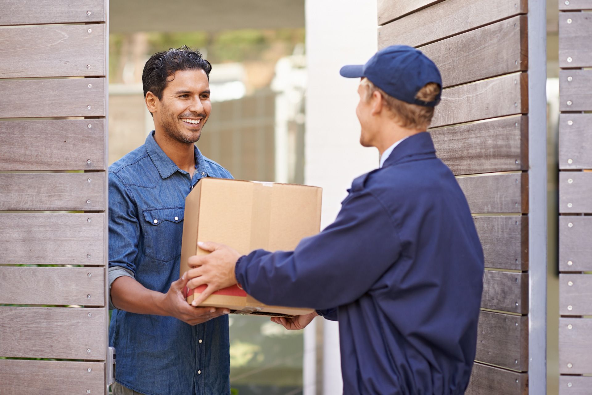 A delivery man is handing a box to a man in a doorway.