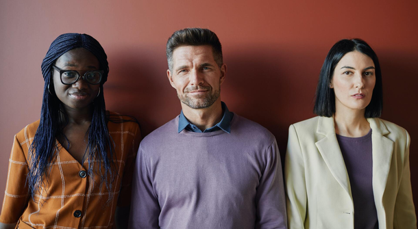 Three people are standing next to each other in front of a red wall.