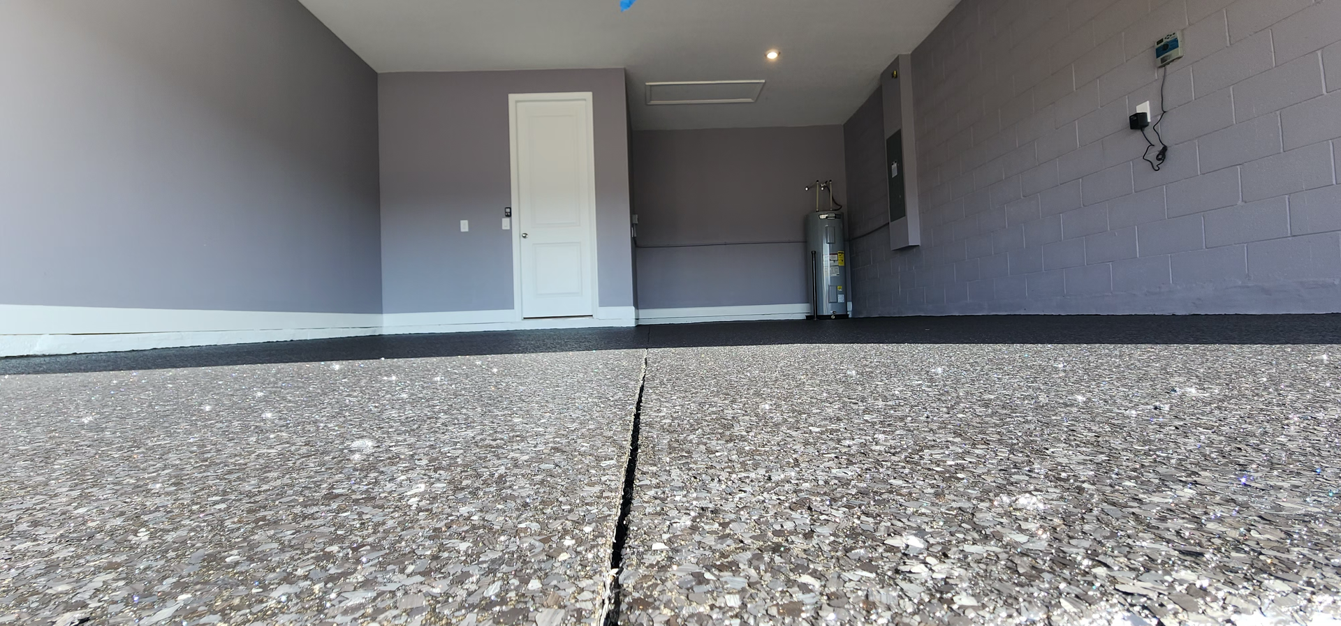 A garage interior with gray walls and a speckled floor. A door is visible in the back, along with what looks like a metal tank.