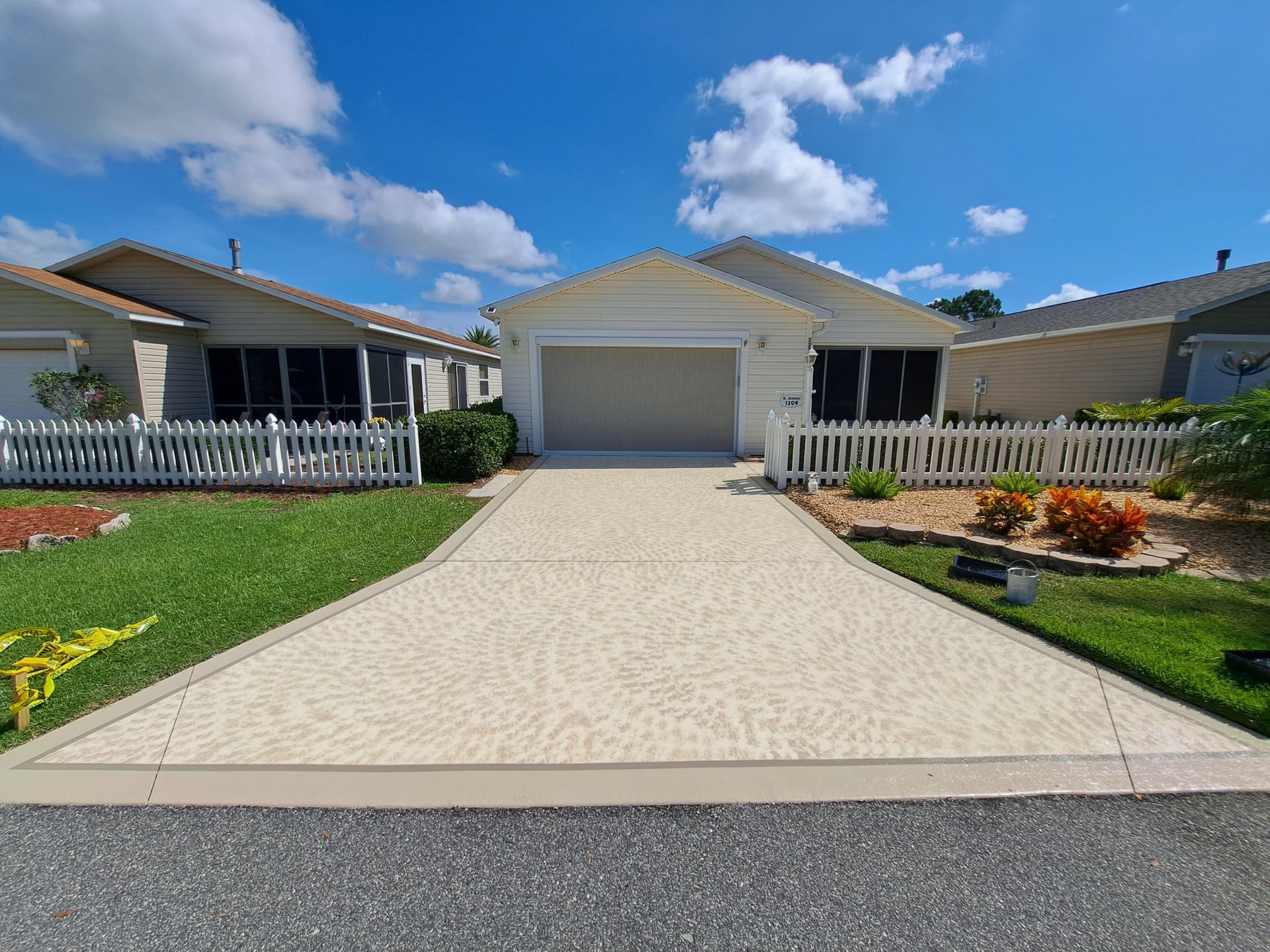 A driveway leading to a house with a garage and a white picket fence.