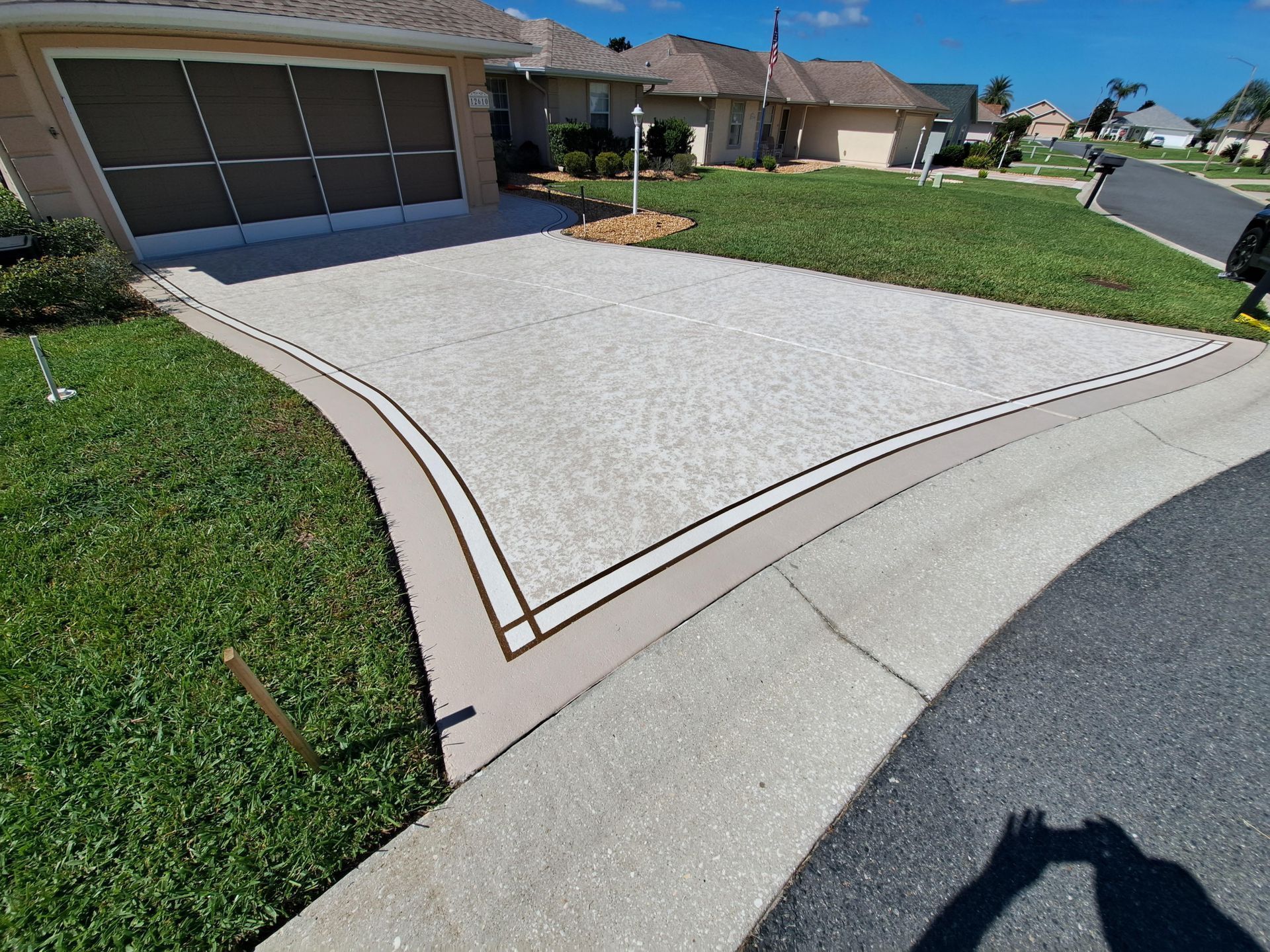 A shadow of a person is cast on a concrete driveway in front of a house.