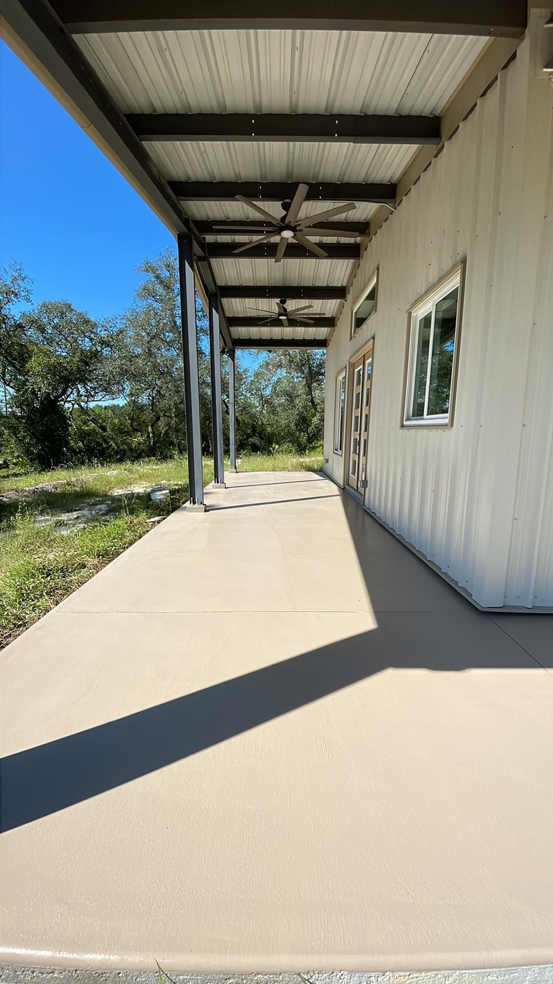 A long walkway leading to a white building with a ceiling fan.