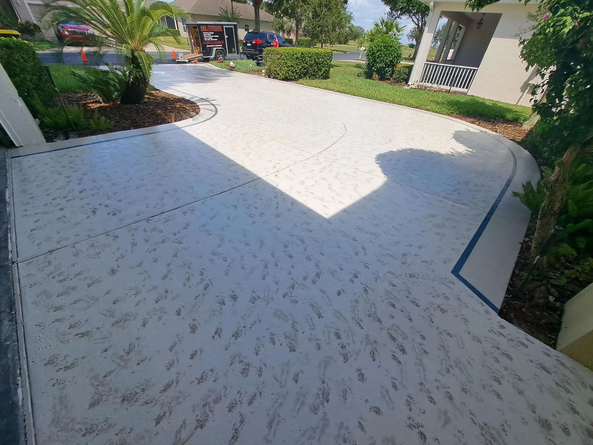 A white concrete driveway with a blue stripe on the side of it leading to a house.