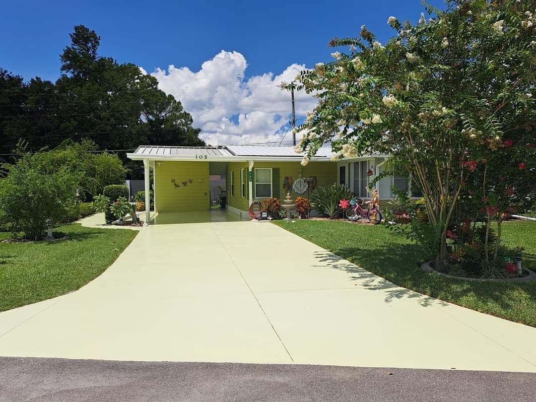 A yellow house with a driveway and trees in front of it.
