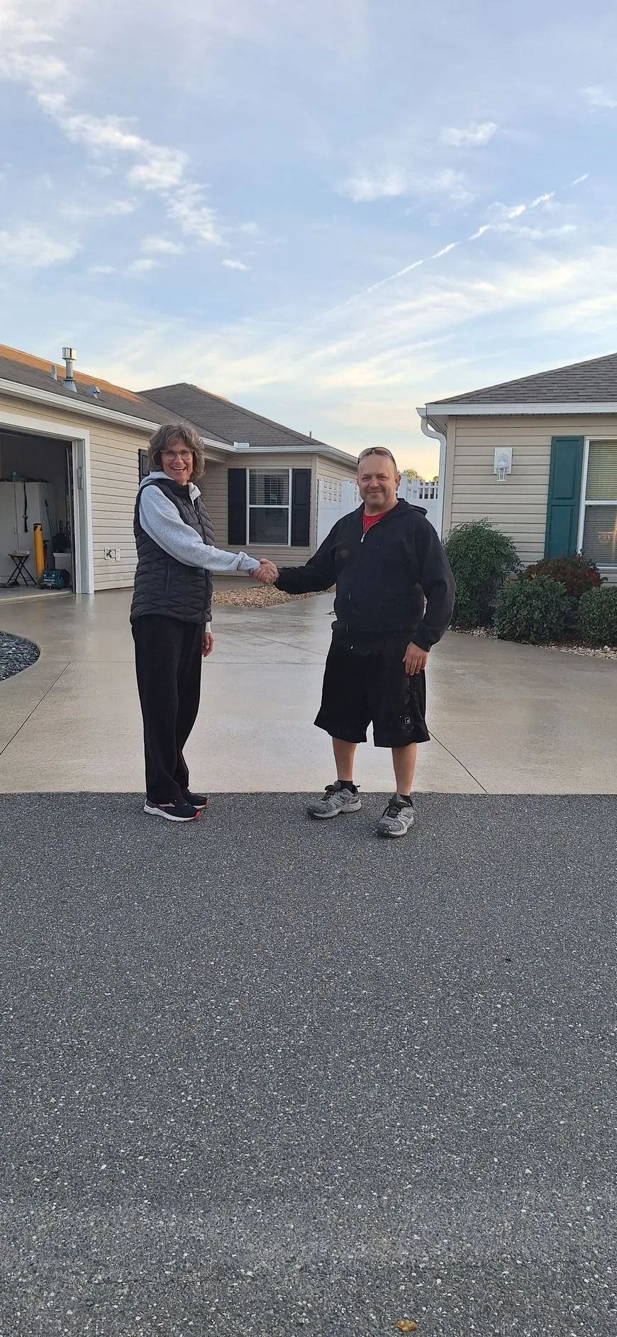 A man and a woman are shaking hands in front of a house.