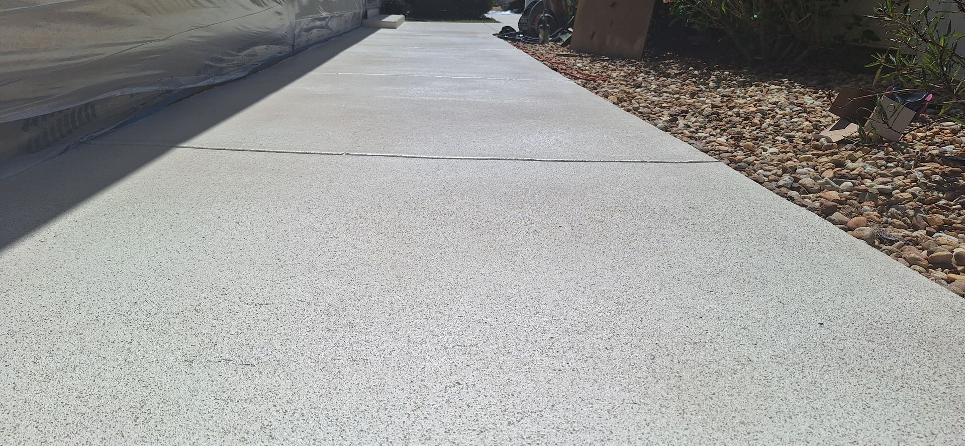 A concrete walkway leading to a house with a tree in the background.