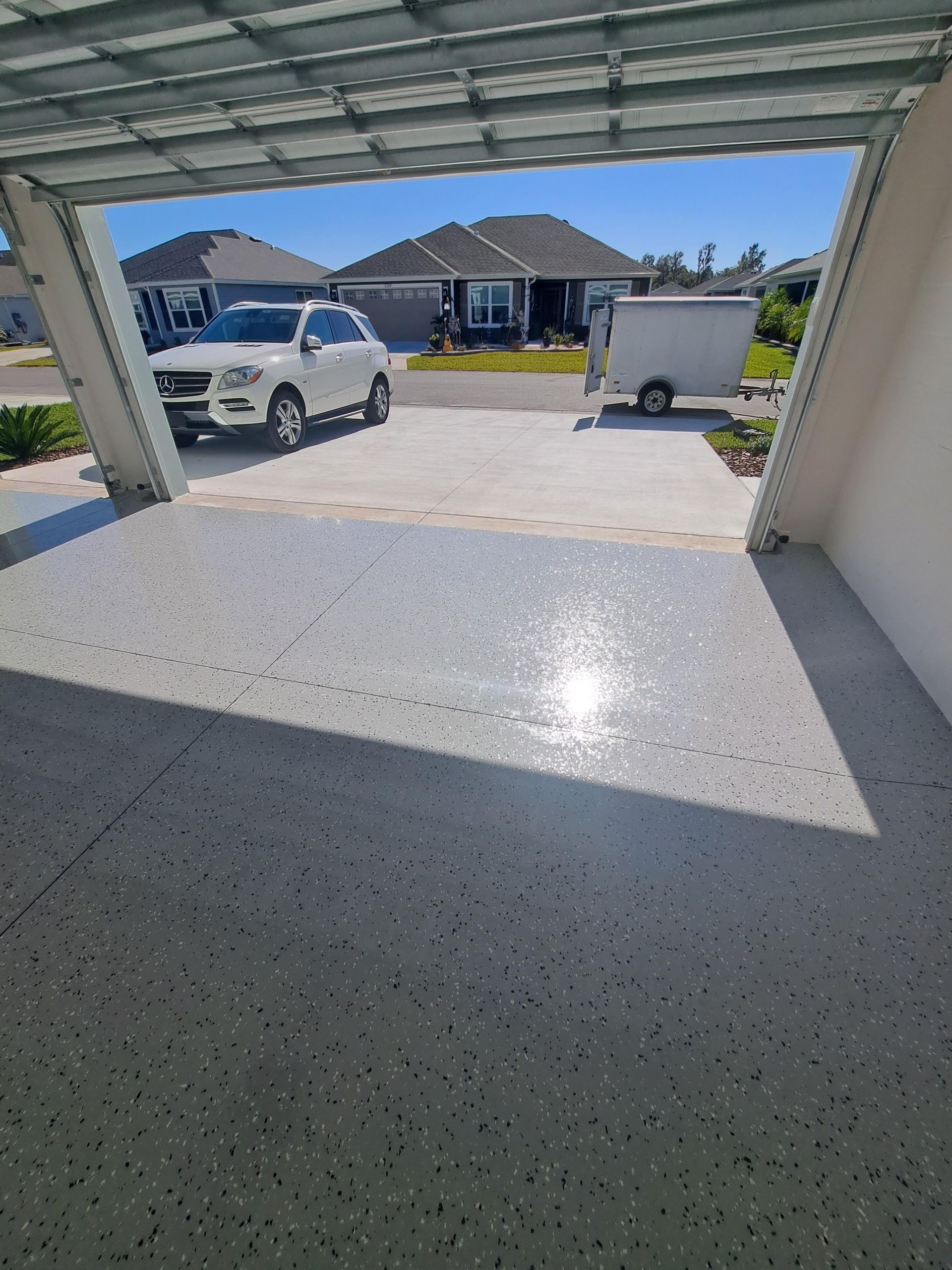 A white car is parked in a garage next to a trailer.