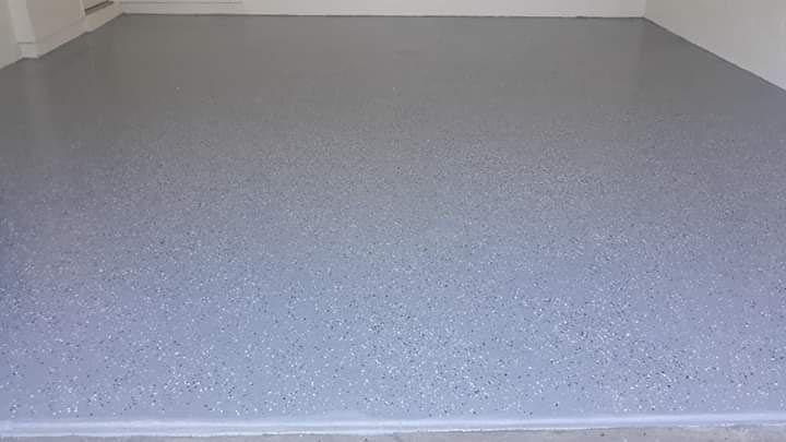 A gray concrete floor in a garage with a white wall.