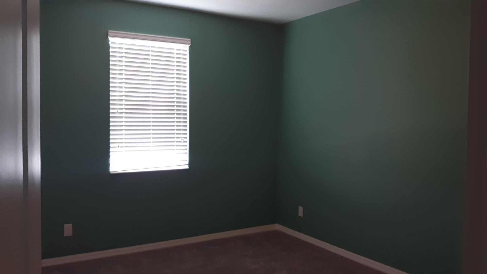 An empty bedroom with green walls and a window with blinds.
