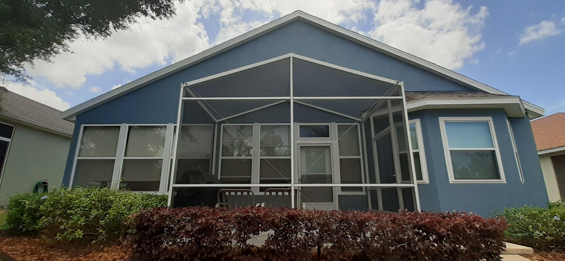 A blue house with a screened in porch and a white roof.